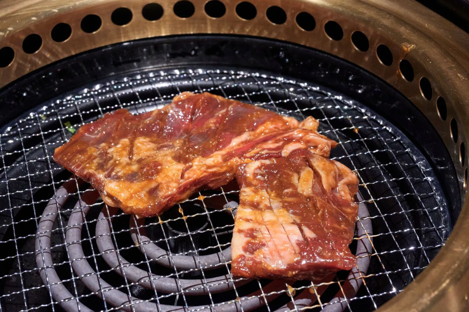 Two pieces of marinated beef short ribs laid on metal barbecue grill mesh at Feast Utopia Clackamas, an Asian Fusion Restaurant in Clackamas