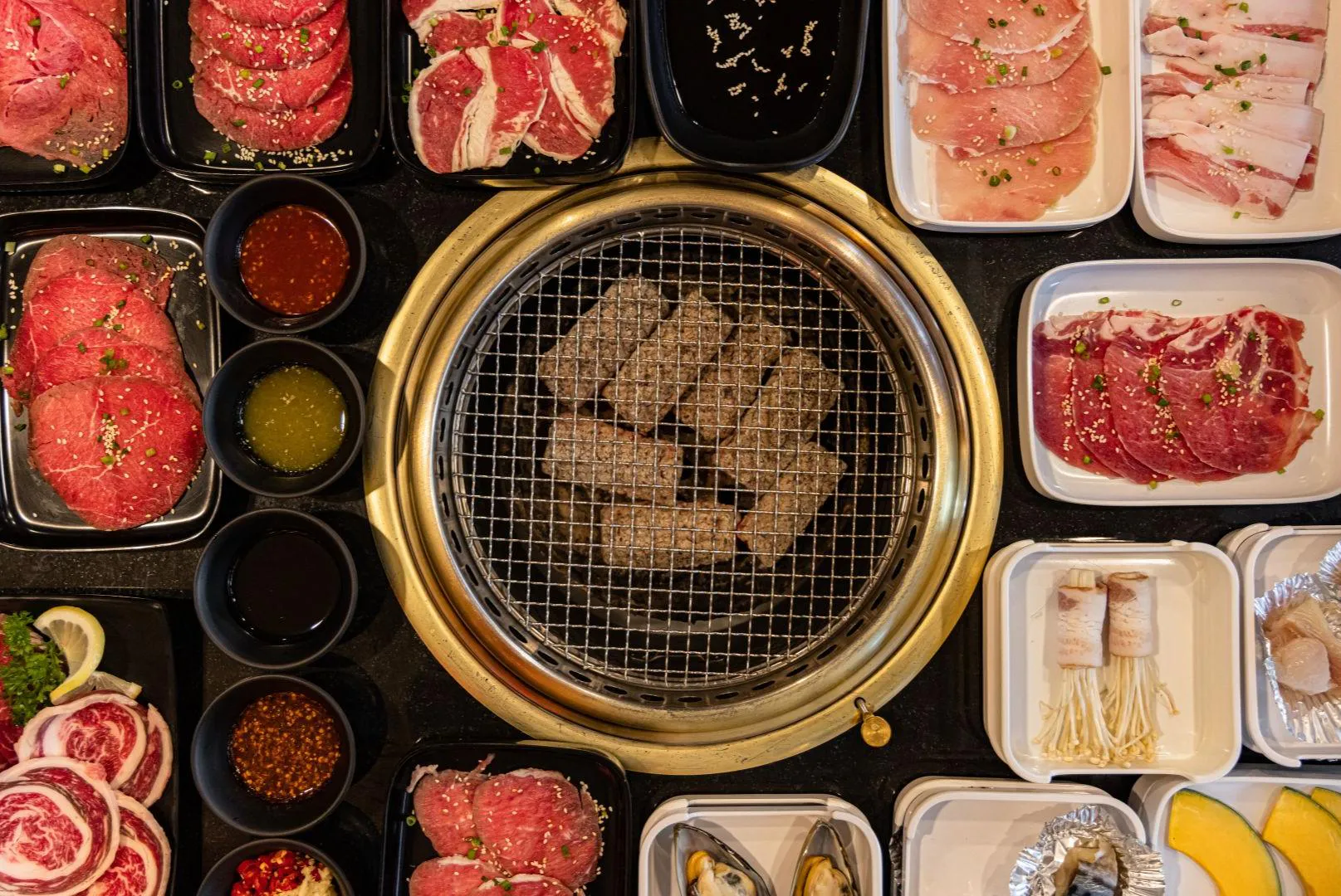 Top-down view full Korean BBQ platter with assorted raw meats, seafood and dipping sauces at Feast Utopia Clackamas, an Asian Fusion Restaurant in Clackamas