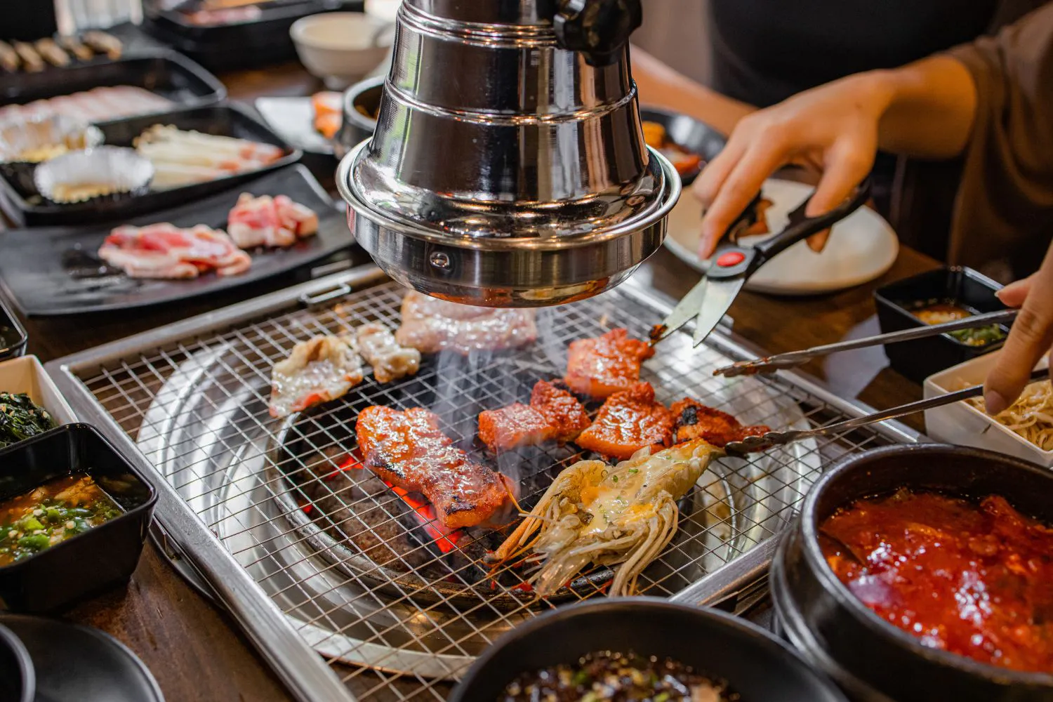 Korean BBQ grill with marinated pork, shrimp and assorted side dishes being cooked at Feast Utopia Clackamas, an Asian Fusion Restaurant in Clackamas