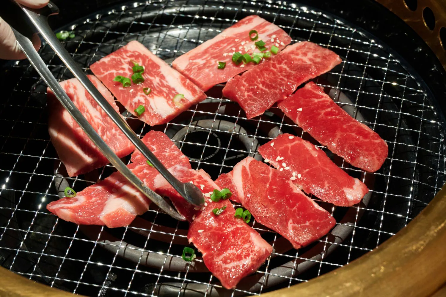 Raw marbled beef slices topped with green onions cooking on Korean barbecue mesh at Feast Utopia Clackamas, an Asian Fusion Restaurant in Clackamas