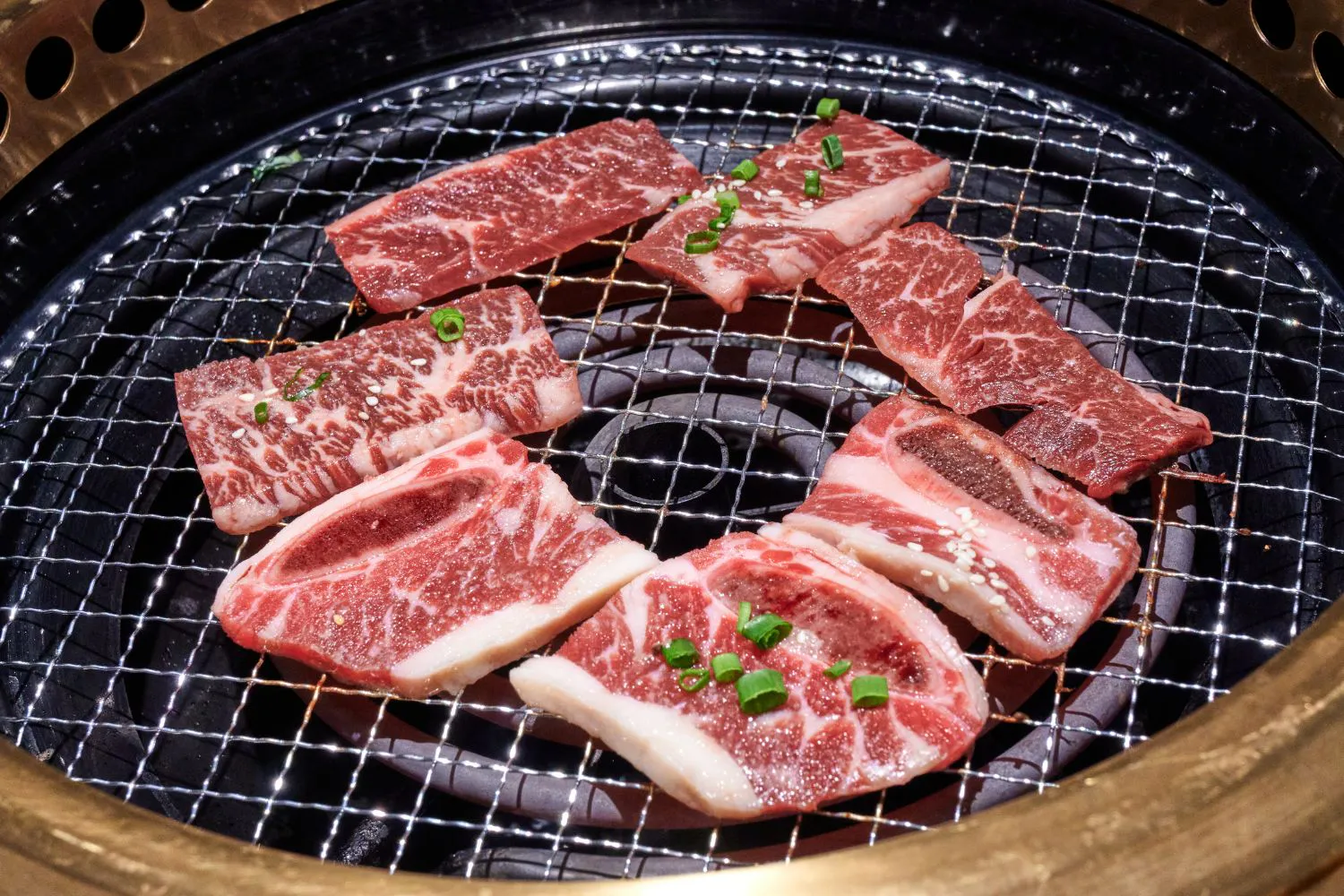 Marbled beef short rib slices garnished with green onion on metal BBQ grill at Feast Utopia Clackamas, an Asian Fusion Restaurant in Clackamas